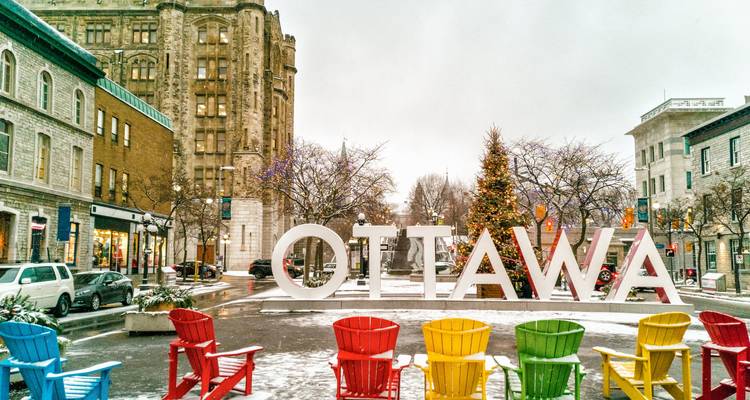 Snow-dusted street with large OTTAWA sign and colorful Adirondack chairs in winter.