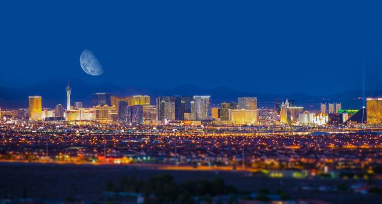 Night panorama of the Las Vegas Strip illuminated under a deep blue sky with a large moon rising.