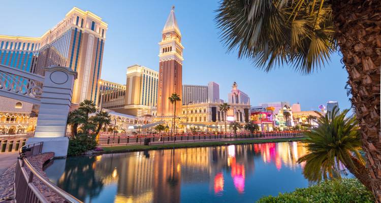 Reflections of The Venetian resort and other hotels along an artificial canal at dusk in Las Vegas.