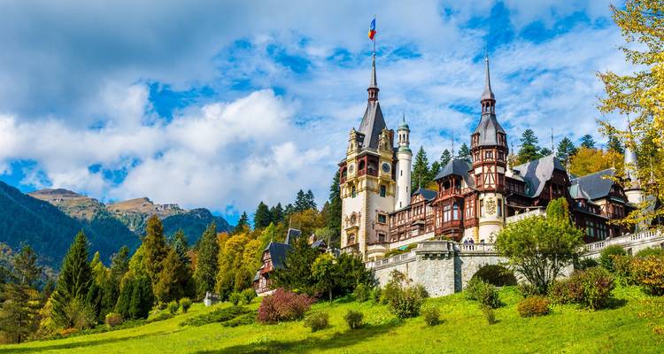 Elegantes Schloss im Neorenaissance-Stil vor bewaldeten Bergen unter einem leuchtend blauen Himmel.