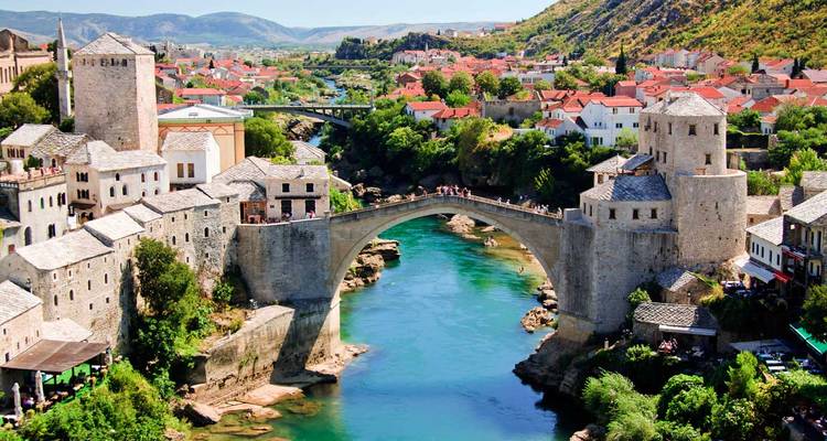 Ikonische gewölbte Steinbrücke, die einen türkisfarbenen Fluss zwischen historischen Steingebäuden in einer Tallandschaft überquert.
