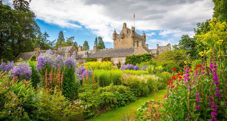 Charmant château écossais entouré de jardins d'été vibrants sous un ciel lumineux.