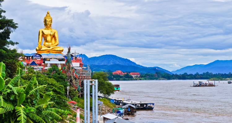 Grand statue de Bouddha doré surplombant le Mékong avec des collines luxuriantes et les temples du Triangle d'Or.