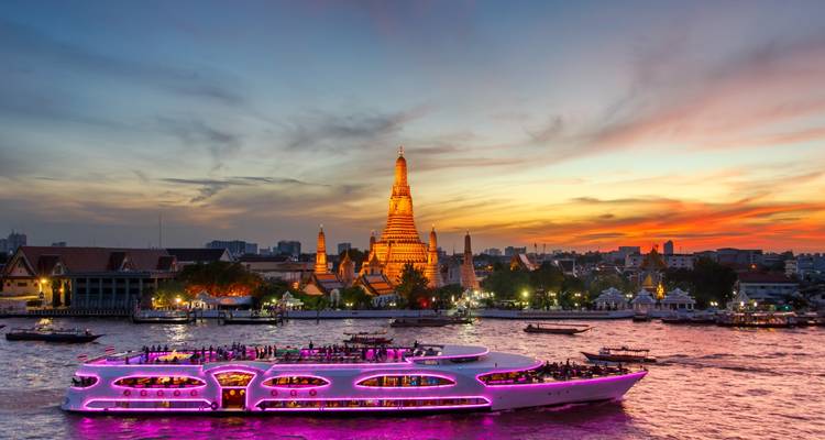 Bateau-restaurant illuminé passant devant le Wat Arun au coucher du soleil sur le fleuve Chao Phraya de Bangkok.