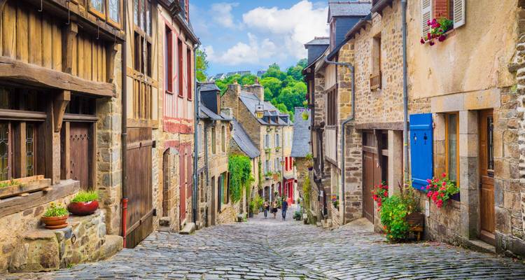 Ruelle pavée de galets escarpée flanquée de maisons médiévales à colombages descendant vers la campagne verdoyante.