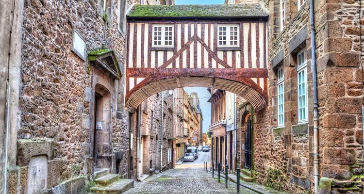 Ruelle médiévale pittoresque en pierre traversée par une maison-passerelle à colombages dans une ville historique.