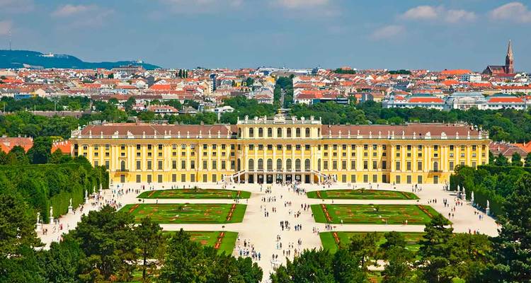 Das prächtige gelbe Schloss Schönbrunn und seine formalen Gärten von oben an einem sonnigen Tag.