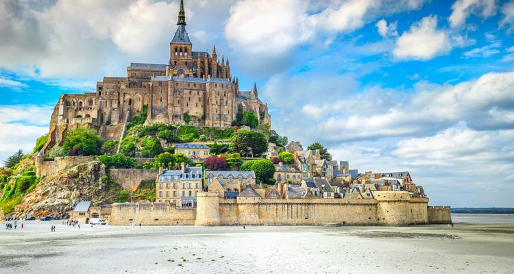 Mont Saint-Michel elevándose sobre enormes llanuras arenosas bajo unas nubes espectaculares