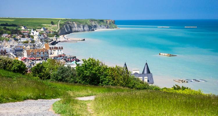 Vue depuis une falaise surplombant la mer turquoise, les champs verdoyants et la station balnéaire d'Arromanches-les-Bains.