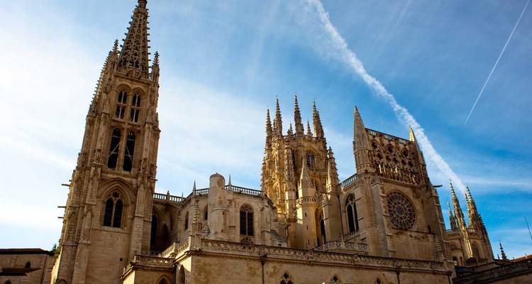 The soaring gothic towers and ornate façade of Burgos Cathedral set against a bright blue sky.