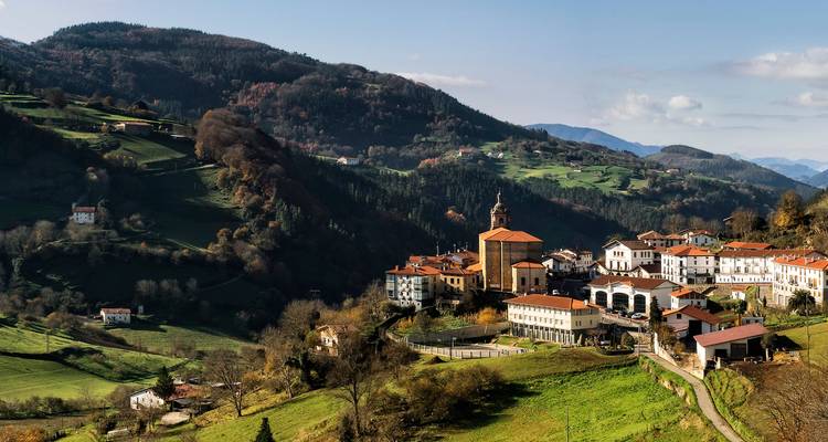 Quiet mountain village with terracotta rooftops nestled among rolling green hills and forested slopes.