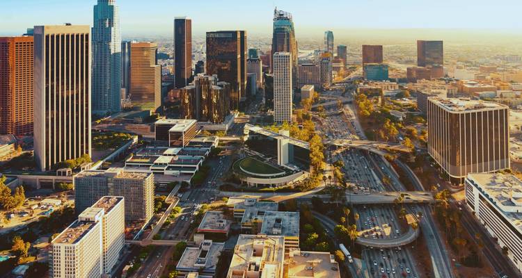 Aerial view over downtown Los Angeles with sprawling freeways and skyscrapers in warm afternoon light.
