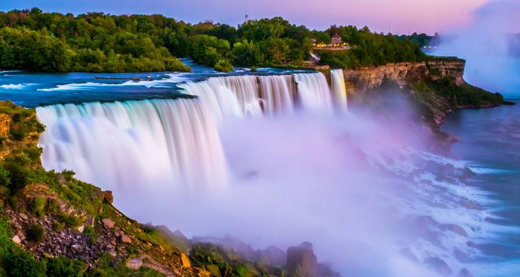 Dramatic sunset view of Niagara Falls with mist rising and vibrant colors in the sky.
