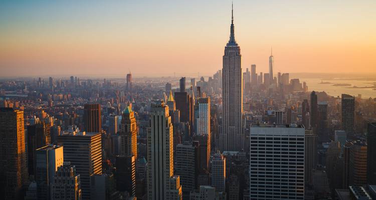 Iconic New York skyline at sunset with the Empire State Building glowing amid vast cityscape.