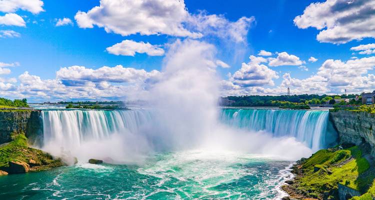 Spectacular Horseshoe Falls with massive mist plume under vivid blue sky and green cliffs.