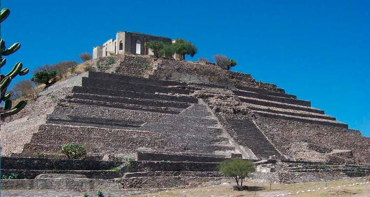 Pyramidenähnliche archäologische Struktur aus Stein mit einer kleinen Kolonialkapelle auf der Spitze unter tiefblauem Himmel