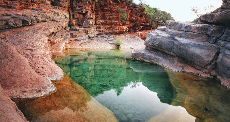 Smaragdgrüner natürlicher Pool, umgeben von roten und grauen Canyonwänden, die das Grün von oben widerspiegeln.
