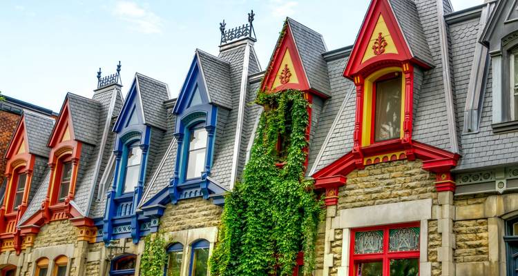 Row of colorful Victorian gabled townhouses with ivy climbing stone walls under blue sky in Montreal.