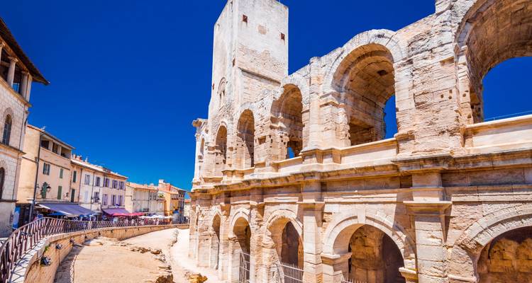 Close view of the Roman amphitheatre in Arles under a vivid blue Provençal sky.