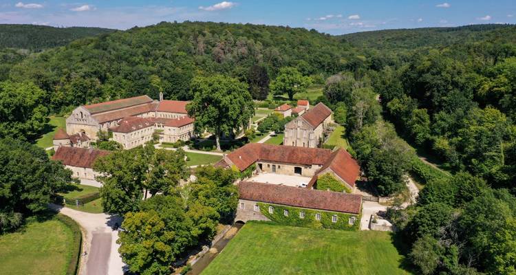 Aerial view of a secluded historic abbey complex surrounded by dense forested hills.