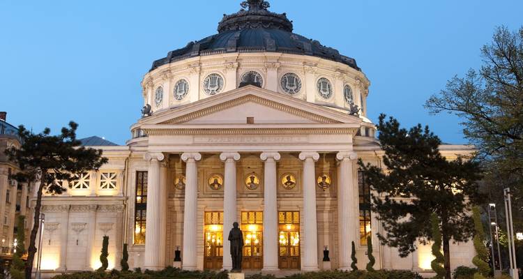 Neoclassical Romanian Athenaeum lit softly at dusk with clear blue twilight sky.