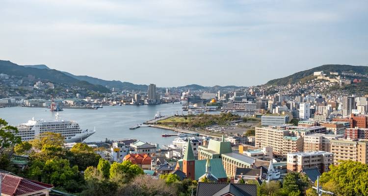 Harbor view of Nagasaki with cruise ship, cityscape, and surrounding hills in afternoon light.