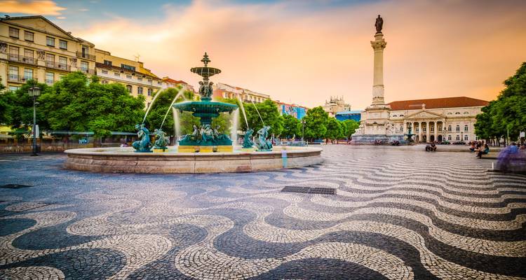 Rossio Square’s swirling mosaic pavement and grand fountain at sunset with pastel sky.