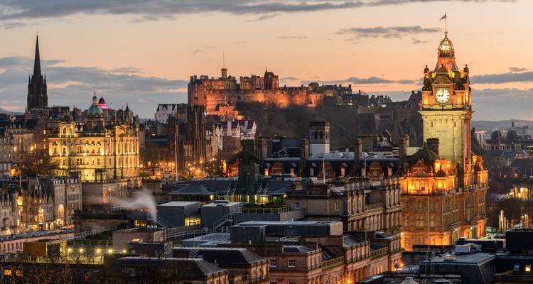 Edinburgh cityscape at dusk with Balmoral Clock Tower and Edinburgh Castle glowing