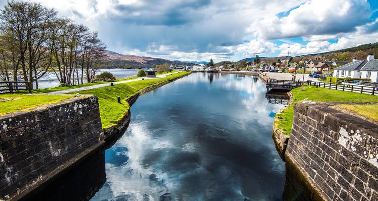 Tranquil section of Caledonian Canal with stone locks, calm water and mountains beyond
