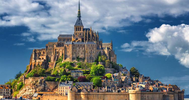 L'abbaye majestueuse du Mont-Saint-Michel s'élève au-dessus d'un village fortifié sur un ciel dramatique parsemé de nuages.