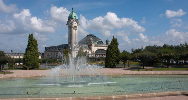 La gare Art-déco Limoges-Bénédictins avec son dôme en cuivre vert se dresse derrière une fontaine animée et des jardins soignés.