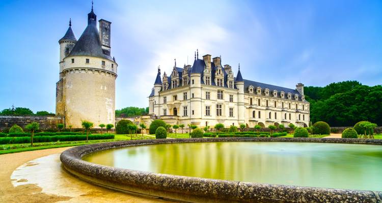 Elegante Château de Chenonceau junto a un estanque circular bien cuidado y exuberantes jardines bajo un cielo suave.