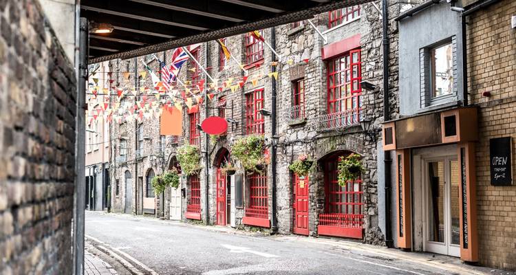 Quiet cobblestoned lane lined with stone façades, bright red doors, hanging bunting and Union Jack flags.