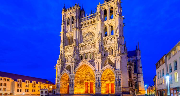 Gothic façade of Amiens Cathedral glowing with warm lighting against a deep twilight sky.