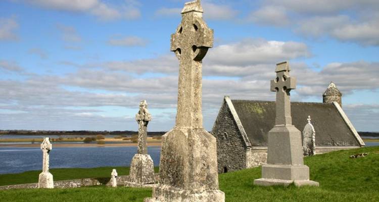 Ancient Celtic stone crosses and a small stone church overlooking a tranquil river and open skies.