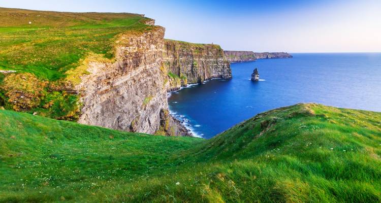 Dramatic green cliffs plunging into the Atlantic Ocean under a soft blue evening sky.