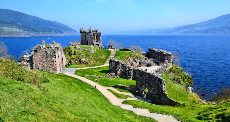 Ruins of a lakeside castle stretching along a grassy promontory into deep blue water.
