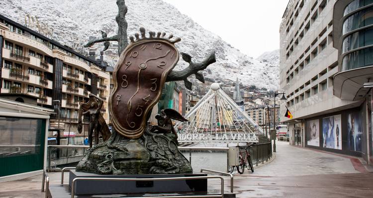 Dalís Skulptur der schmelzenden Uhr im verschneiten Andorra la Vella mit alpinen Gebäuden und Bergen