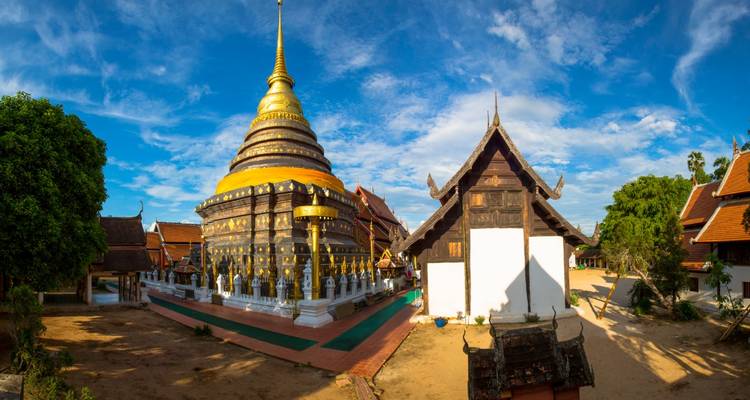 Vue panoramique du Wat Phra That Lampang Luang avec son chedi doré et ses bâtiments en teck sous des cieux bleus.