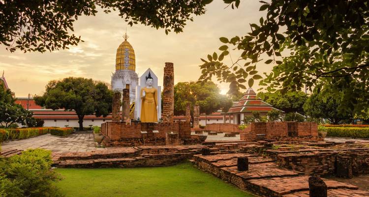 La statue du Bouddha debout s'élève au-dessus des ruines de briques anciennes et d'un chedi doré au coucher du soleil.
