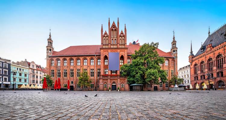 Grand red-brick Gothic town hall dominates the spacious cobbled market square of Torun at dawn.