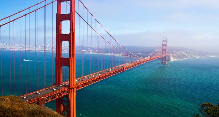 A sweeping view of the iconic red Golden Gate Bridge spanning turquoise waters toward the distant San Francisco skyline.