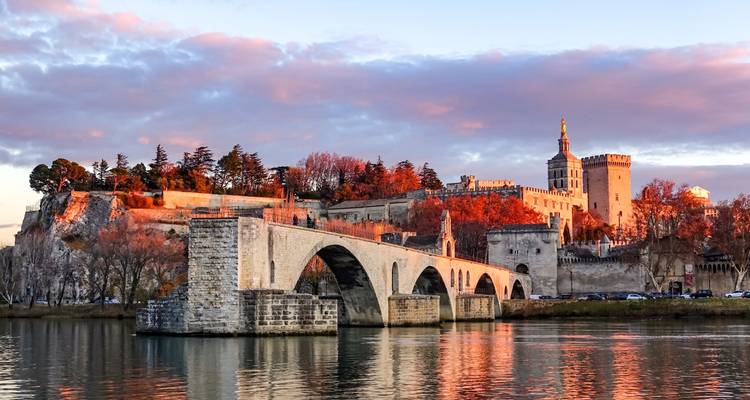 La lumière dorée du coucher de soleil sur le pont de pierre médiéval d'Avignon avec le Palais des Papes et les arbres d'automne se reflétant dans le Rhône.