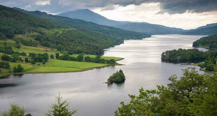 Serene loch stretching into the distance flanked by rolling green hills and forest, seen from above.