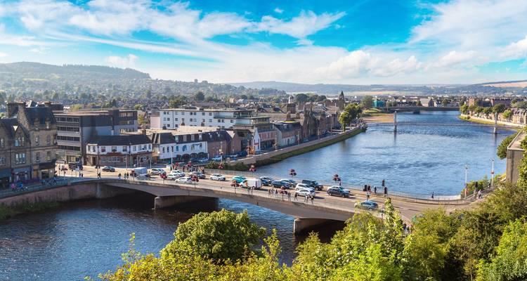 Bridge over the River Ness and colorful buildings of Inverness under a bright sky.