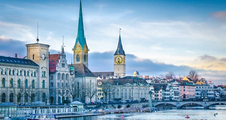 Skyline classique de Zurich avec les tours de la Fraumünster et de Saint-Pierre surplombant la rivière Limmat sous une lumière crépusculaire aux tons pastel.