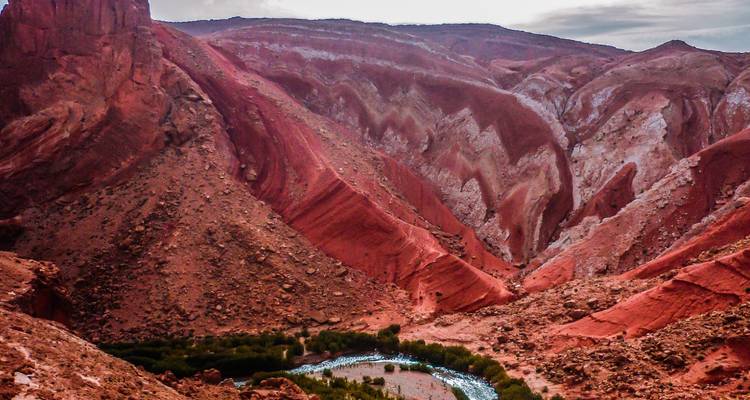 Les parois du canyon aux rayures dramatiques rouges et roses plongent vers une boucle de rivière verte bien en dessous.