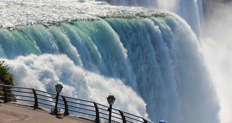 Een machtige watermuur stort neer over de Niagarawatervallen met mist en uitkijkplatformen eronder.
