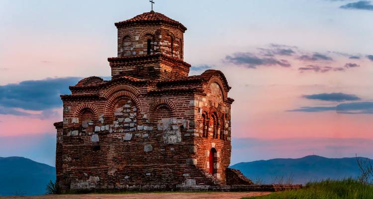 Small solitary brick Byzantine church on a hill at dusk with pastel sky.