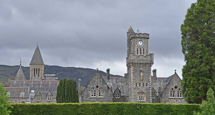 Stone abbey with clock tower set against grey skies and mountain backdrop in Fort Augustus.